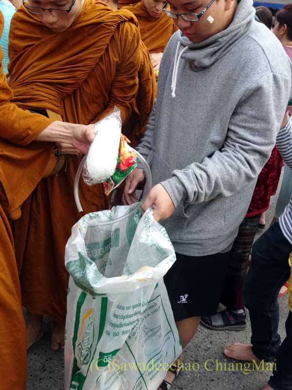 チェンマイの元旦の特別タムブンで供養物をずだ袋に入れる僧侶